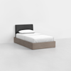 A minimalist single bed with a dark gray upholstered headboard, white bedding, and a light wood frame sits in an empty, light gray room.