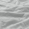 A close-up of a light gray, quilted fabric blanket with visible stitching and soft, gentle folds.