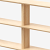 Close-up view of a light wood bookshelf with vertical and horizontal panels intersecting in a minimalist, grid-like design against a plain background.
