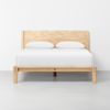 A minimalist wooden bed frame with a headboard, made of light-colored wood, is shown with a white mattress and two white pillows against a plain white wall.