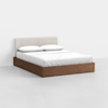 A modern bed with a light beige upholstered headboard, white bedding, and a wooden platform base, set against a plain white background.