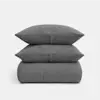 A neatly stacked set of dark gray textured bedding, including two pillows placed on top of a folded quilt, against a plain white background.