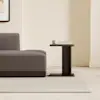 A modern, dark wood nightstand sits next to a matching bed frame with white bedding in a minimalist room with white walls and a light floor.