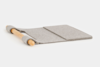 A wooden rolling pin rests on top of a flat, rectangular gray felt mat with a crease down the middle, forming a simple kitchen tool on a white background.