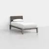 A minimalist single bed with a light wood frame, a dark upholstered headboard, and white bedding, placed in a bright, empty room with a light gray floor and white walls.