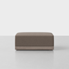 A rectangular, brown upholstered ottoman with a low wooden base, placed on a light gray floor against a plain white background.