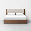 A modern wooden bed frame with a light upholstered headboard, topped with two white pillows and white bedding, set against a plain white wall and gray floor.