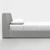 A side view of a modern, minimalist bed with a light gray upholstered frame, white bedsheet, and a single white pillow, set against a plain white background.