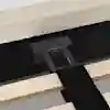 Close-up of a bed frame showing a black metal support bracket attached to the headboard, with wooden slats and a black fabric strap visible in the foreground.