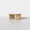 A modern, round, light wood coffee table with a flat top and three wide, flat legs, set against a plain white background.