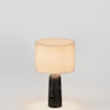 A cylindrical table lamp with a dark, marbled stone base and a warm, glowing fabric drum shade.