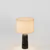A cylindrical table lamp with a dark, marbled stone base and a warm, glowing fabric drum shade.