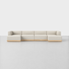 A modern, light beige sectional sofa with low, wide seats and wood trim at the base, set against a plain white background and placed on a smooth, light gray floor.