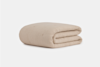 A folded, light beige quilted blanket with a textured, grid-like pattern, displayed against a plain white background.