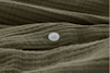 Close-up of a white, four-hole button sewn onto textured, olive-green fabric with visible ridges and folds.