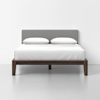 A modern bed with a dark wooden frame, a gray upholstered headboard, and crisp white bedding with two pillows, set against a plain white background.