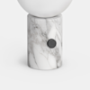A lamp with a white spherical top sits on a cylindrical marble base featuring gray veining and a round black knob on the side.