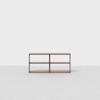 A simple, modern wooden shelf unit with four open compartments, placed against a plain white background on a light gray floor.