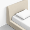 A beige upholstered bed with a tall, cushioned headboard and white bedding, including a pillow and sheet, positioned on a light gray floor against a white wall.