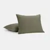 Two olive green square pillows with a visible stitched grid pattern, one upright and the other lying flat, on a plain light background.