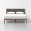 A modern bed with a wooden frame, a dark upholstered headboard, white sheets, and two white pillows, set against a plain white wall and floor.