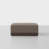 A square, brown upholstered ottoman with a dark wooden base, placed on a light gray floor against a plain white background.