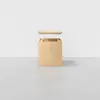 A light wooden box with a square shape is shown with its lid floating above, revealing an empty interior. The box sits on a smooth gray surface against a plain white background.