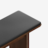 A close-up view of a wooden bench with a dark gray upholstered cushion on top, shown against a plain white background.
