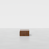 A minimalist wooden box-shaped table sits on a smooth, white surface against a plain white background.