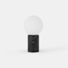 A minimalist table lamp with a round white frosted glass bulb on top of a cylindrical black marble base, set against a plain white background.