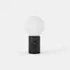 A minimalist table lamp with a round white frosted glass bulb on top of a cylindrical black marble base, set against a plain white background.