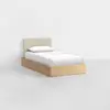 A minimalist single bed with a light wood frame, white bedding, a single pillow, and a beige upholstered headboard, set against a plain white background.