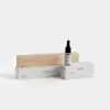 Minimalist product display featuring a wooden box, a dropper bottle labeled Deep Forest, and two white rectangular boxes with text, all set against a plain white background.