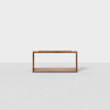 A minimalist wooden rack with a rectangular frame and open sides, placed on a light gray surface against a plain white background.