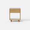 A minimalist wooden nightstand with a single drawer and an open shelf at the bottom, placed on a light gray floor against a plain white background.