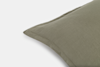 A close-up of a green pillow with a simple, textured fabric and visible stitching, set against a plain white background.