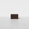 A minimalist, dark wooden rectangular box with clean lines sits centered on a smooth, light gray surface against a plain white background.