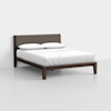 A modern wooden bed frame with a brown upholstered headboard, dressed with white bedding and two white pillows, set in a minimal, empty room with light gray floors and white walls.