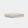 A neatly folded, light beige quilt or blanket is placed on a plain white surface with a minimalist background.