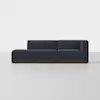 A modern, dark blue sectional sofa with low backrests and armrests, set on a wooden base, placed in a minimalistic, light-colored room.