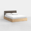 A modern wooden platform bed with a dark upholstered headboard, neatly made with white sheets, two pillows, and a white comforter, set against a plain white background.