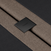 Close-up of two brown textured fabric straps secured by a black metal piece with the word THUMA engraved, placed on a dark background.