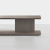 A modern, minimalist wooden bench or low table with a rectangular top and base connected by a central vertical support, all in a smooth gray-brown finish, set against a plain white background.