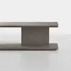 A modern, minimalist wooden bench or low table with a rectangular top and base connected by a central vertical support, all in a smooth gray-brown finish, set against a plain white background.