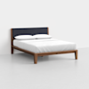 A modern wooden bed frame with a dark upholstered headboard, neatly made with white bedding and two white pillows, set against a plain white background.