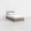 A minimalist single bed with a light gray upholstered headboard, white bedding, and a wooden platform base, set against a plain white wall and floor.