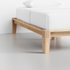 A close-up of a wooden bed frame with four sturdy legs, supporting a neatly made bed with white sheets and a white pillow, set on a smooth, light-colored floor.