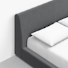 A modern bed with a dark gray upholstered headboard and frame, featuring white pillows and a neatly made white sheet, set against a light-colored wall and floor.
