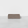 A rectangular, light brown wooden box with an open top sits on a smooth, light gray surface against a plain white background.