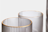 Two clear glass cups with vertical ribbed texture and thin gold rims are shown against a plain white background.